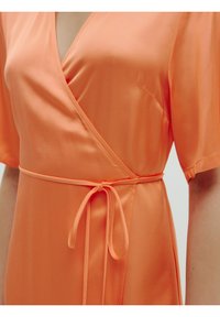 Wikkeljurk van feloranje stof, met een V-hals, korte mouwen en een strikceintuur in de taille. Soepele, lichtgewicht textuur.