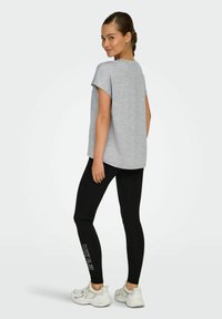 T-shirt grigio a maniche corte abbinato a leggings neri con testo sulla parte bassa della gamba. Il modello indossa scarpe da ginnastica bianche.