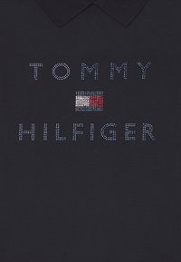 Námořnická polokošile s textem "TOMMY HILFIGER" vyrobeným z bílých rhinestonů a malým designem vlajky v červené, bílé a modré barvě.