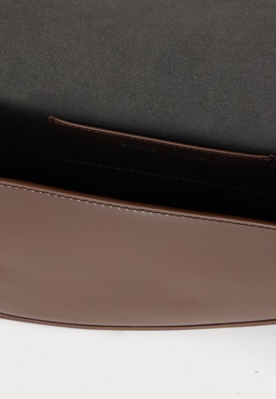 Gros plan d’un sac en cuir marron ouvert avec des coutures lisses et une doublure intérieure foncée montrant une petite poche intérieure.