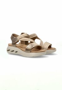Sandalias beige con acentos metálicos dorados, correas cruzadas y una suela ergonómica con recortes para ventilación. Plantilla de textura suave.