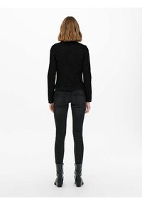 Veste en denim noir au design ajusté, avec une fermeture à boutons à l'avant et deux poches latérales. Portée avec un jean noir et des bottines.