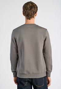 Sudadera gris con cuello redondo y puños acanalados. Textura de tela suave con un ajuste relajado, vista desde la parte de atrás. Combinada con jeans oscuros.