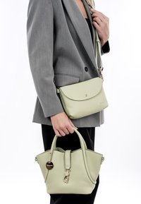 Borse in pelle verde chiaro: una tracolla con pattina e hardware dorato, e una tote più piccola e strutturata con doppi manici e un charm.