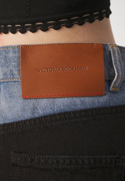 Pantalons en denim avec un design contrasté noir et bleu clair. Présente une étiquette en cuir marron embossée avec "Victoria Beckham" et des coutures rouges.