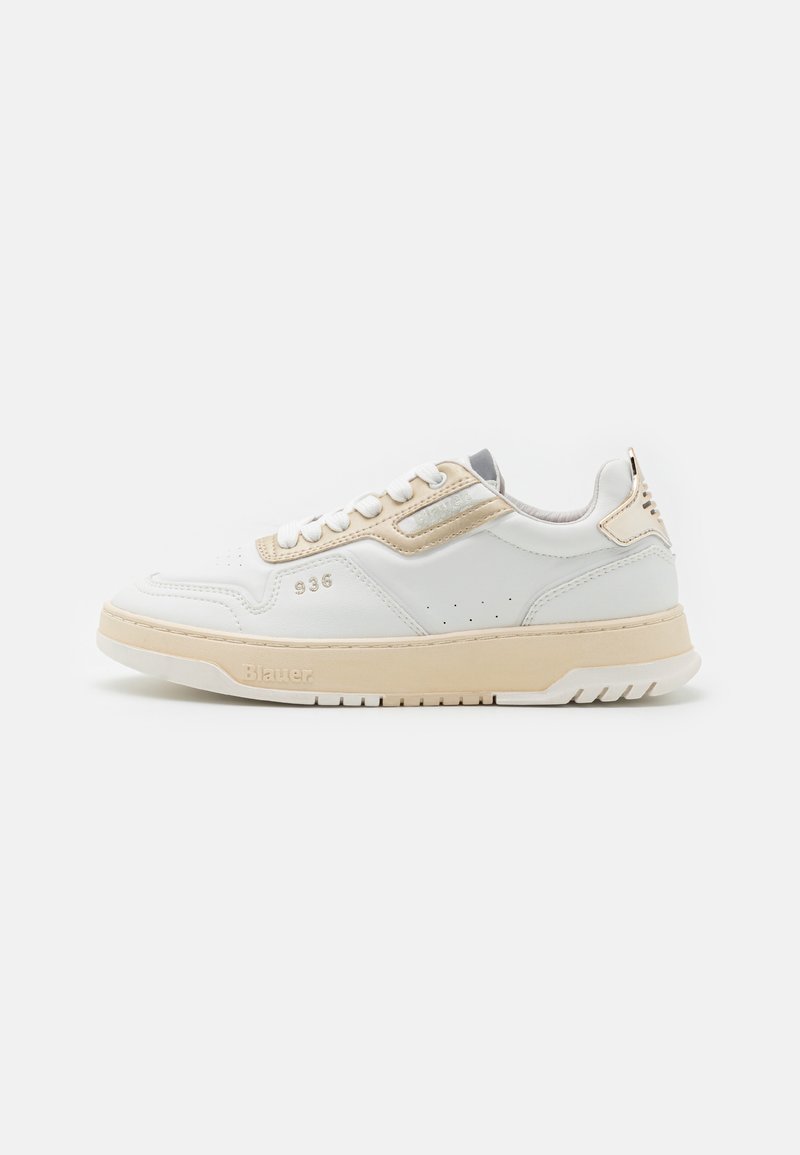 Baskets basses blanches avec accents beige, lacets blancs, détails perforés et semelle beige sur un fond clair uni.