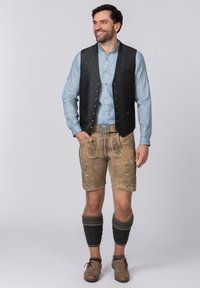 Lederhosen shorts in beige with green floral embroidery, paired with a light blue shirt and a black, textured vest. Completed with gray knitted socks.