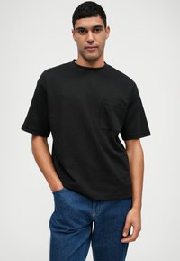 Μαύρη κοντομάνικη μπλούζα με στρογγυλή λαιμόκοψη και τσέπη στο αριστερό στήθος. Συνδυασμένη με μπλε τζην παντελόνι.