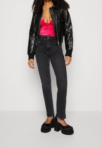 Giubbotto bomber in pelle nera, top in satin rosa, jeans neri a vita alta e chunky platform neri. Trame morbide e design aderente.