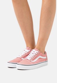 Baskets en toile rose avec des lacets blancs, des rayures latérales blanches et une semelle en caoutchouc avec une ligne accent noire le long du bord.