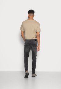 Tan kortærmet t-shirt kombineret med mørkegrå slim fit jeans og grå sko, der viser et minimalistisk design og en glat tekstur.