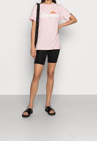 Rosa bomull t-shirt med "ellesse" logotyp, i kombination med svarta cykelbyxor och svarta sandaler. Inga mönster, minimalistisk design.