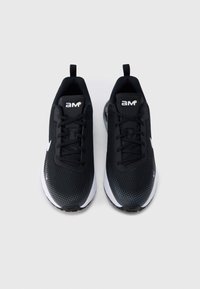 Ζευγάρι μαύρα και λευκά αθλητικά παπούτσια με κορδόνια, με το λογότυπο "am" στη γλώσσα, εμφανίζονται από πάνω σε φωτεινό φόντο.