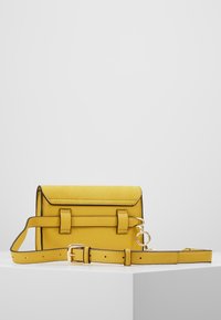Borsa a tracolla gialla in pelle con due cinturini frontali, accessori in oro e tracolla regolabile. Texture liscia con bordi in contrasto.