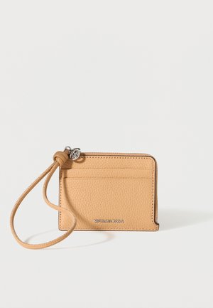 Kartica Michael Kors iz teksturirane usnjene kože rjave barve z zadrgo, zapestnim trakom in srebrnim logotipom spredaj na enobarvnem ozadju.