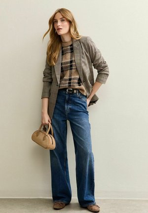Grijze geruite blazer over een beige geblokte trui, gecombineerd met wijde blauwe jeans. Accessoires zijn een kleine tan handtas en bruine schoenen.