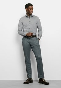 Gray button-up shirt, tailored fit, long sleeves. Light gray textured fabric. Dark gray trousers, standard fit. Black leather shoes, polished finish.