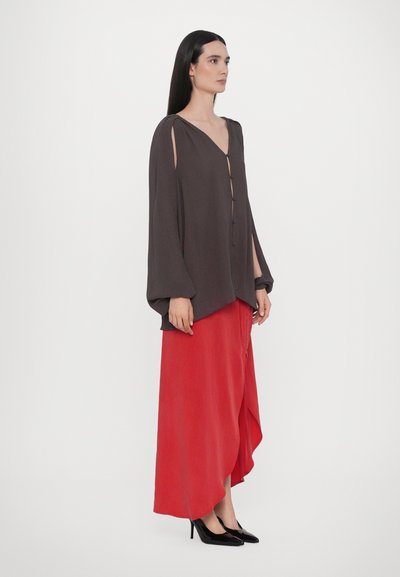 Schwarze Bluse mit langen Ärmeln und Knopfverschluss, kombiniert mit einem fließenden roten Maxirock. Schwarze High Heels runden das Outfit ab.