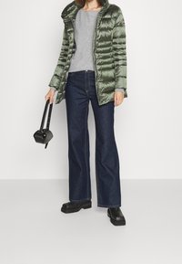 Green padded jacket with a hood, grey sweatshirt, dark blue wide-leg jeans, and black chunky boots. Small black handbag with a strap.