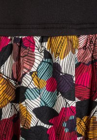 Květinová látka s skládacím designem, která zobrazuje listy v růžové, fialové, tyrkysové a žluté barvě na bílém pozadí a černé horní části.