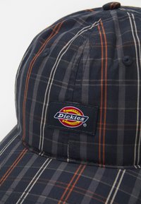 Marine geruite pet van geweven stof, met grijze, oranje en witte strepen. Voorzien van een rechthoekige Dickies-logo patch aan de voorkant.