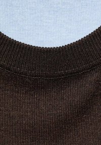 Close-up of ribbed dark brown knitted sweater neckline over light blue textured shirt.