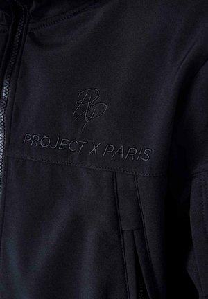 Chaqueta negra con cremallera que presenta una textura suave, con el logo bordado "PROJECT X PARIS" y un emblema estilizado "RP" en el pecho.