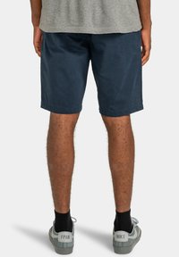 Shorts bleu marine en tissu doux, dotés d'une coupe décontractée et d'un bas ourlé. Portés avec un t-shirt gris et des chaussures de sport grises.