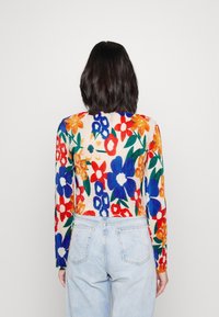 Langärmliges Oberteil aus geripptem Material mit einem mehrfarbigen Blumenmuster, hauptsächlich in Rot, Blau und Orange, kombiniert mit hochgeschnittenen Jeans.