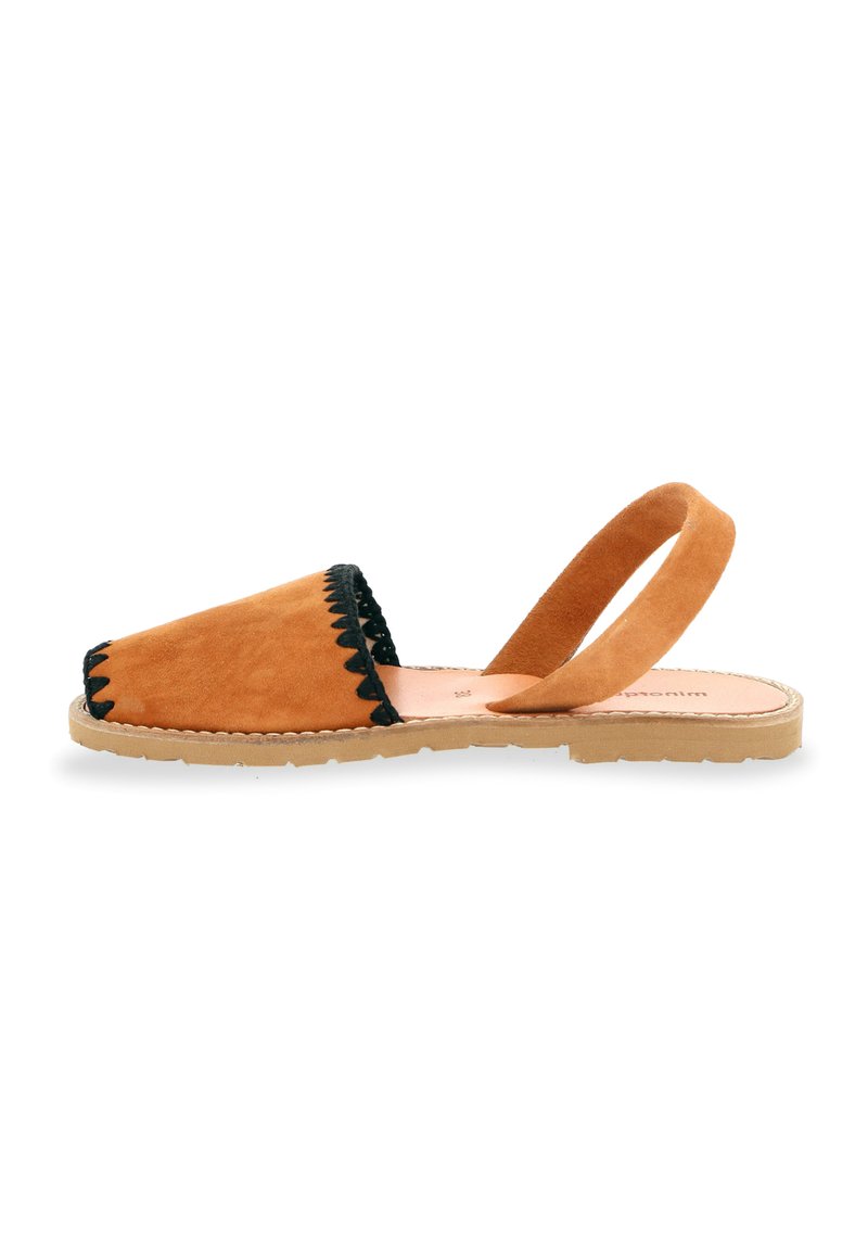 Sandales à enfiler en suède beige avec un contour ondulé noir et une sangle au niveau de la cheville, dotées d'une semelle intérieure en cuir texturé et d'une semelle en caoutchouc durable.