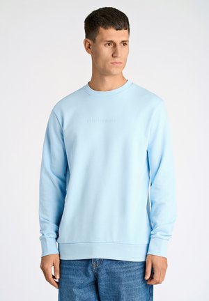 Lys blå sweatshirt med rund hals, lange ærmer, ribbede manchetter og kant. Har præget branding på brystet. Bæres med blå jeans.