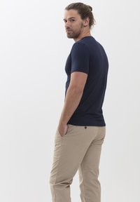 T-shirt bleu marine à manches courtes, design ajusté, fabriqué en tissu lisse. Associé à un pantalon beige clair, avec une poche arrière et un détail de bouton.
