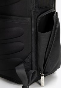 Sac à dos noir avec un extérieur texturé, des sections rembourrées, une poche zippée et une petite étiquette en métal. Fabriqué en tissu durable.
