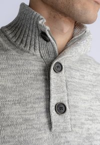 Maglione grigio lavorato a maglia con colletto a coste, dotato di tre bottoni neri e una consistenza morbida, mostrato da vicino sulla scollatura di un modello.