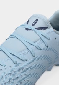 Ghetă de fotbal albastru deschis cu partea superioară texturată din material sintetic, șireturi și un logo mic negru pe limbă.