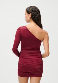 Burgundi vienos peties trumpa suknelė, pagaminta iš elastingos medžiagos, su surinkta tekstūra ir stilinga, prigludusia siluetu.