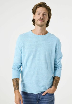 Chemise à manches longues bleu clair en tissu texturé, avec un col rond et une coupe décontractée, associée à un jean en denim.