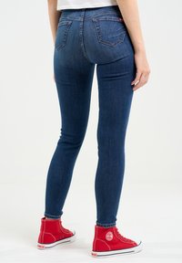 Vaqueros ajustados de denim azul oscuro con una textura suave, con bolsillos traseros y una cintura de altura media, combinados con zapatillas altas rojas brillantes.