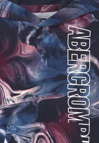 Mikina s kapucí s modro-maroónovým mramorovým vzorem, s bílým logo "ABERCROMBIE" výrazně umístěným na přední straně.
