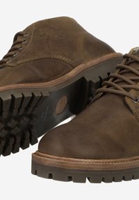 Chaussures en cuir marron avec une semelle extérieure robuste, dotées d'œillets métalliques et de coutures contrastées. Surface texturée ajoutant du détail et de la durabilité.