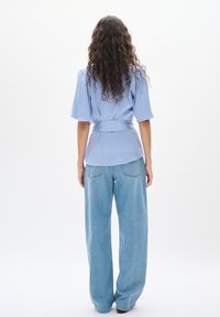 Blusa azzurra chiara con maniche corte e vita cinturata, abbinata a jeans azzurri chiari a gamba larga con tasche posteriori.