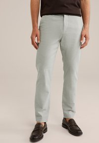 Svetlo zelene, teksturirane hlače s slim fit krojem in ravnim sprednjim delom. Sovpadajo s temnimi loafer čevlji, kar poudarja formalno, a hkrati sproščeno zasnovo.
