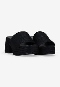 Sandalias de dedo tejidas en negro con una correa ancha y una suela de plataforma gruesa y en capas. La textura es trenzada, con un forro interior suave.