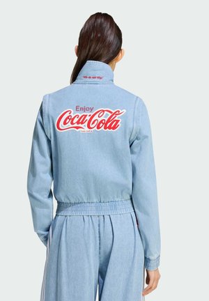 Persona con chaqueta y pantalones de mezclilla azul claro, de espaldas, la chaqueta muestra un gran logo rojo "Enjoy Coca-Cola".