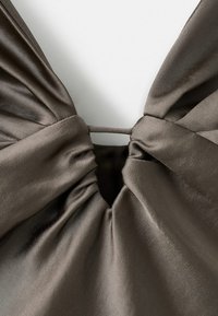 Tejido de satén gris oscuro que forma un escote halter con detalles fruncidos y una abertura central, enfatizando una textura suave y una caída elegante.