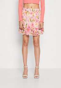 Blommig minikjol i ljusrosa med gröna och gula accenter. Har en volangkant och elastisk midja. Bärs med vita klacksandaler.