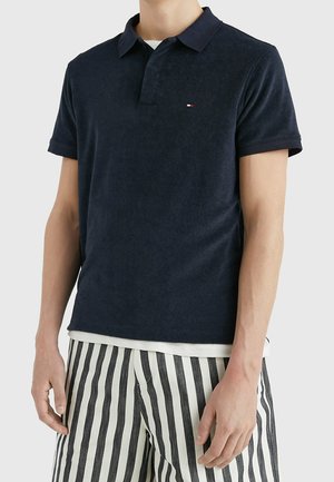 Granatowa koszulka polo z miękkiego materiału typu terry, z klasycznym kołnierzykiem, krótkimi rękawami, subtelnym logo, w zestawie z paskowanymi spodniami.