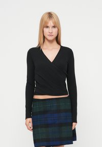 Top negro de manga larga con acabado texturizado, combinado con una falda de cuadros multicolor con tonos verdes y azules.