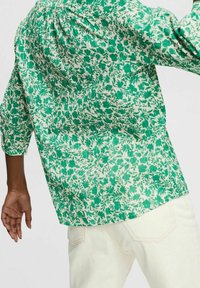 Camicia verde con motivo floreale realizzata in tessuto leggero, caratterizzata da una vestibilità comoda e maniche a tre quarti, abbinata a pantaloni di colore chiaro.