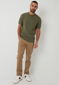 Olijfgroen gebreid truitje met korte mouwen, beige broek en witte sneakers met zwarte accenten, met een gestructureerd patroon en een ronde hals.